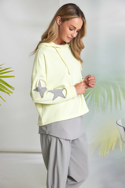 Woman wearing a light yellow hoodie with star designs against a white background.